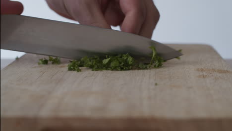 hands cutting parsley with a knife over a chopping board in 4k