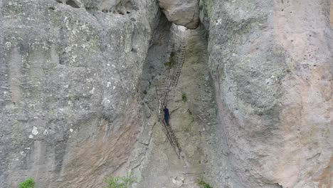 Vista-Por-Drones-De-Un-Hombre-Subiendo-Una-Escalera-En-Karadzhov-Kamak-En-La-Montaña-Ródope,-Bulgaria