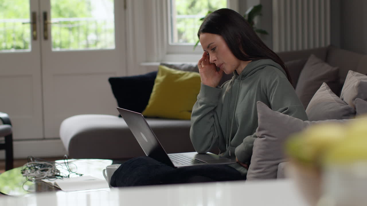 mujer ansiosa sentada en el sofá trabajando desde casa usando una computadora portátil preocupada por la crisis del costo de la vida 4