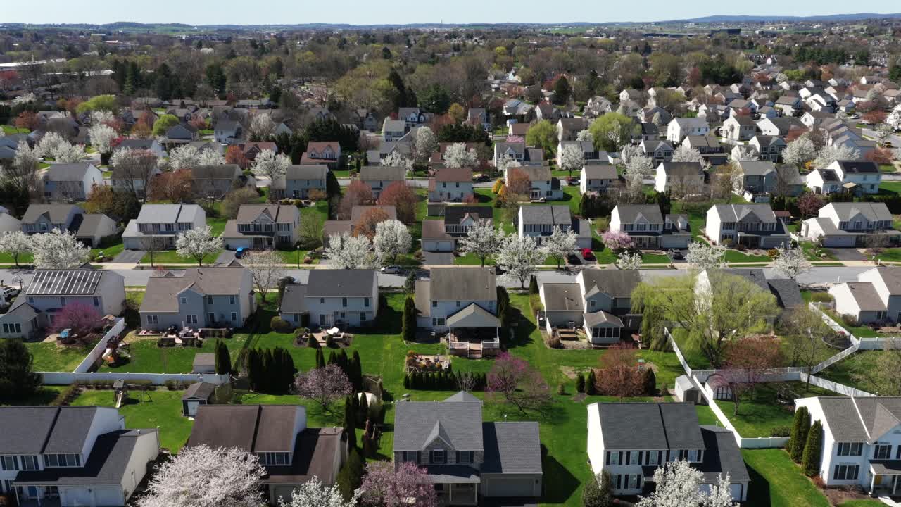 Vista aerea di un grande quartiere residenziale americano con file di case unifamiliari, prati verdi e alberi in fiore in primavera, che mostra una vita residenziale pacifica e una pianificazione urbana organizzata. Sorvolo