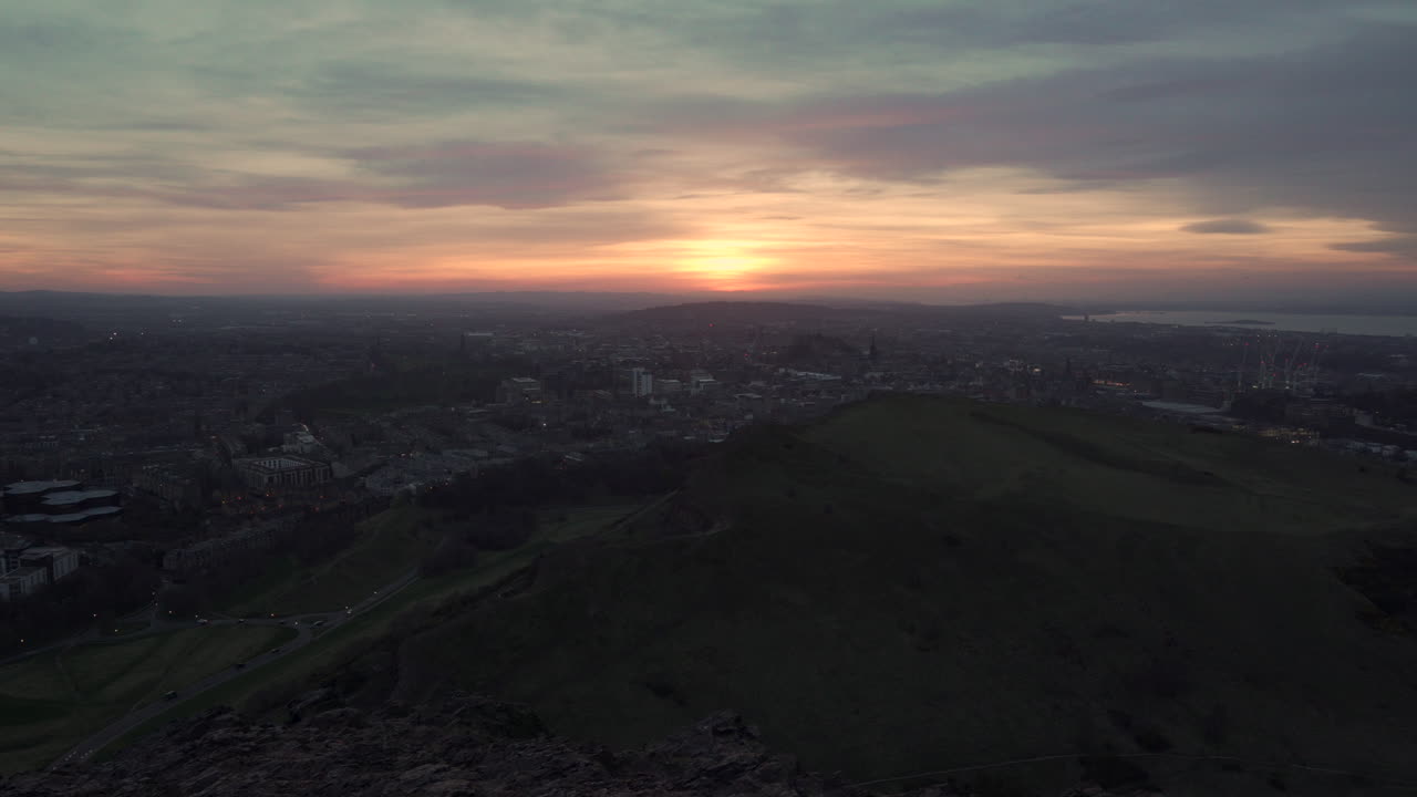 tomada estática del paisaje urbano de edimburgo desde la montaña momentos después de la puesta de sol desde el asiento de arthur con una maravillosa puesta de sol, luz azul de la hora con coches que pasan por abajo