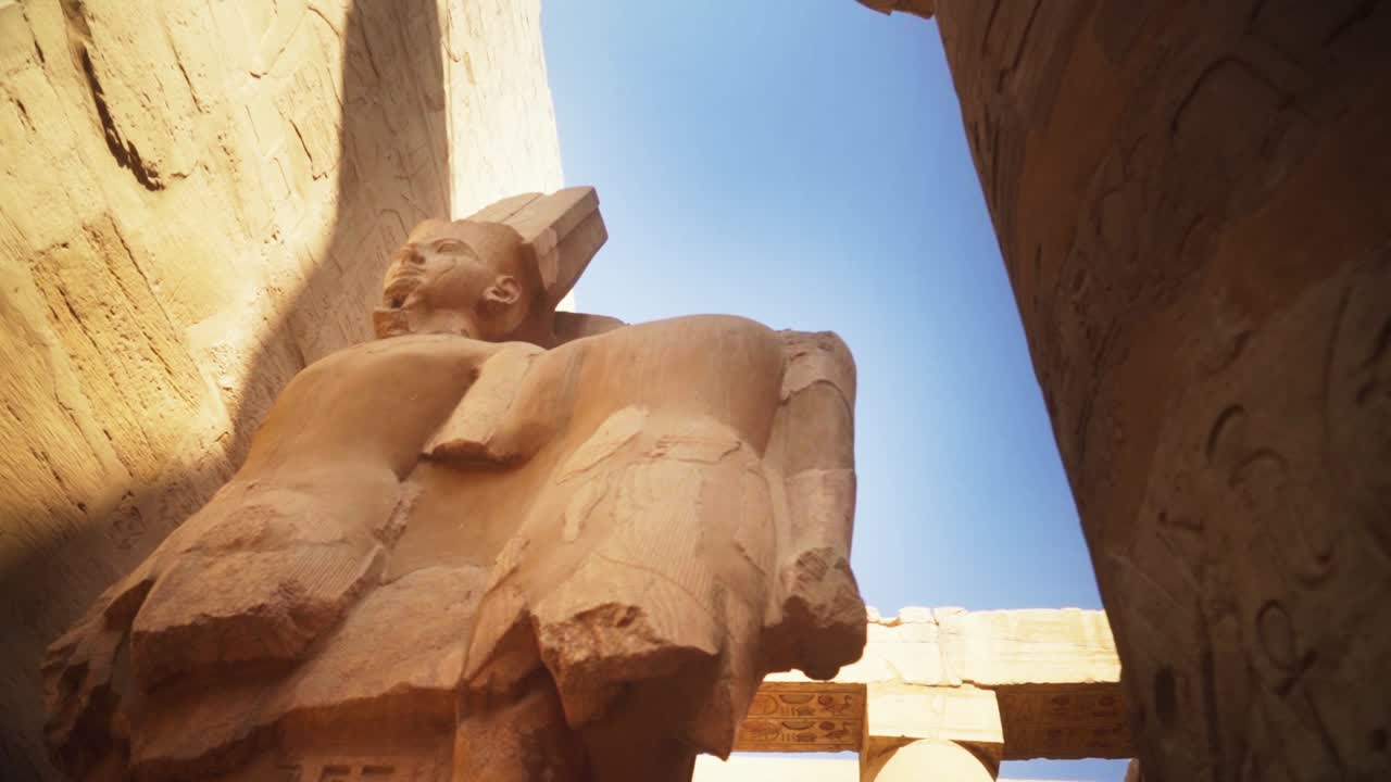 Statue of King Ramses in the Karnak Temple, Luxor Egypt. Slow camera rotation from a low angle, backlit by the sun.