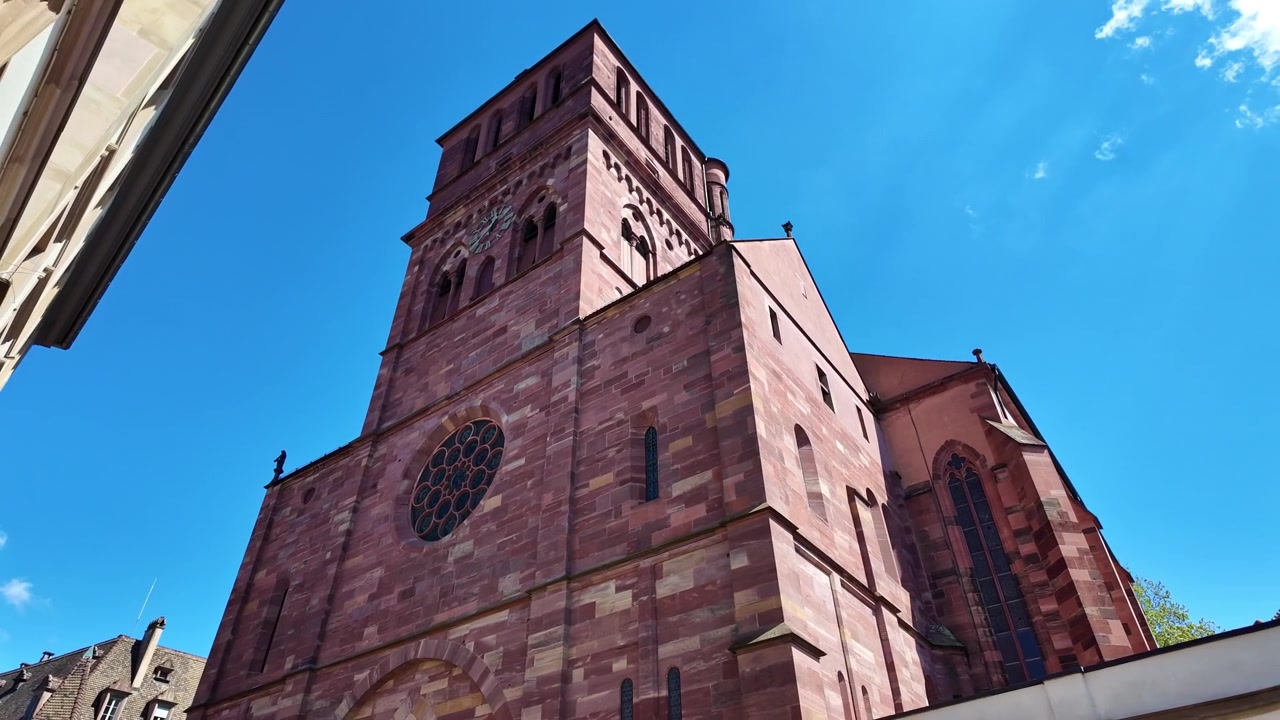 Vista dal basso della facciata in arenaria rossa e della torre dell'orologio della storica Chiesa di San Tommaso contro il cielo blu a Strasburgo, Francia.