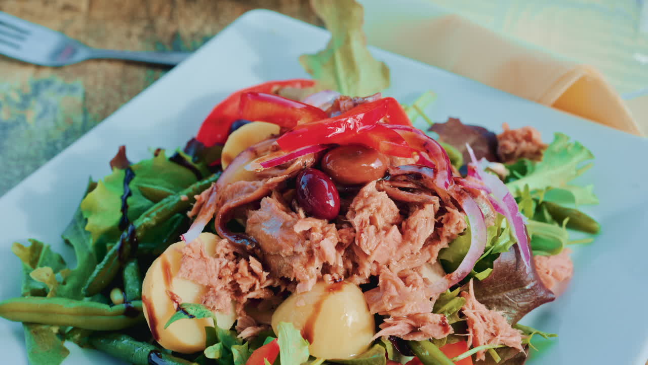 Close up of a colourful salad with tuna, potatoes, olives, red onion, peppers and mixed greens