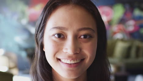 young asian woman smiling to camera in front of mural at creative workplace, head shot, close up