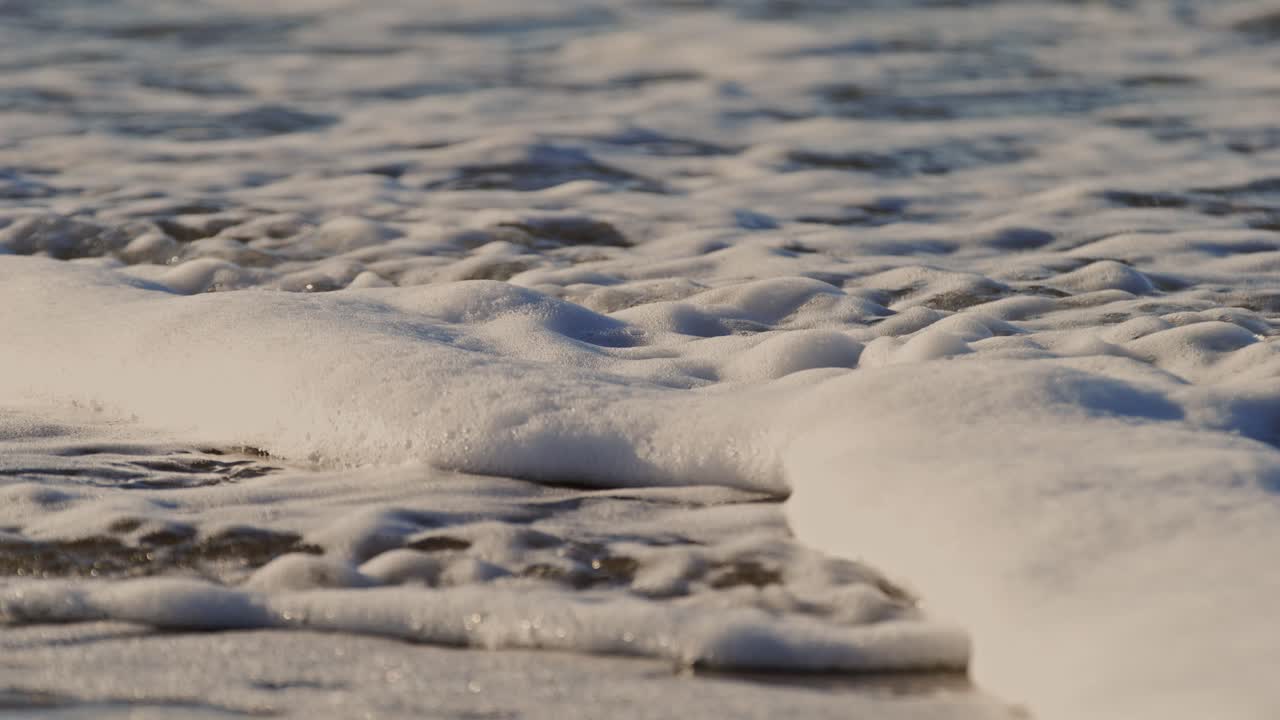 Foamy waves rolling over a sandy beach, super slow-motion near Oosterschelde barrier