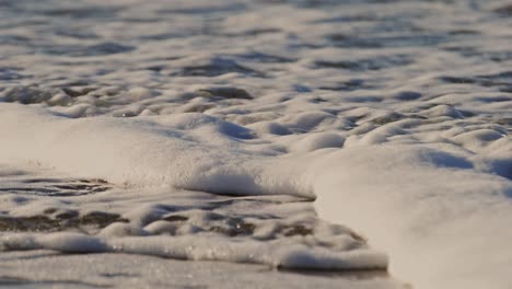 foamy waves rolling over a sandy beach, super slow-motion near oosterschelde barrier