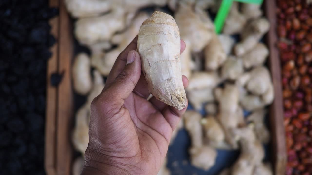 A person's hand holding a piece of ginger at a market