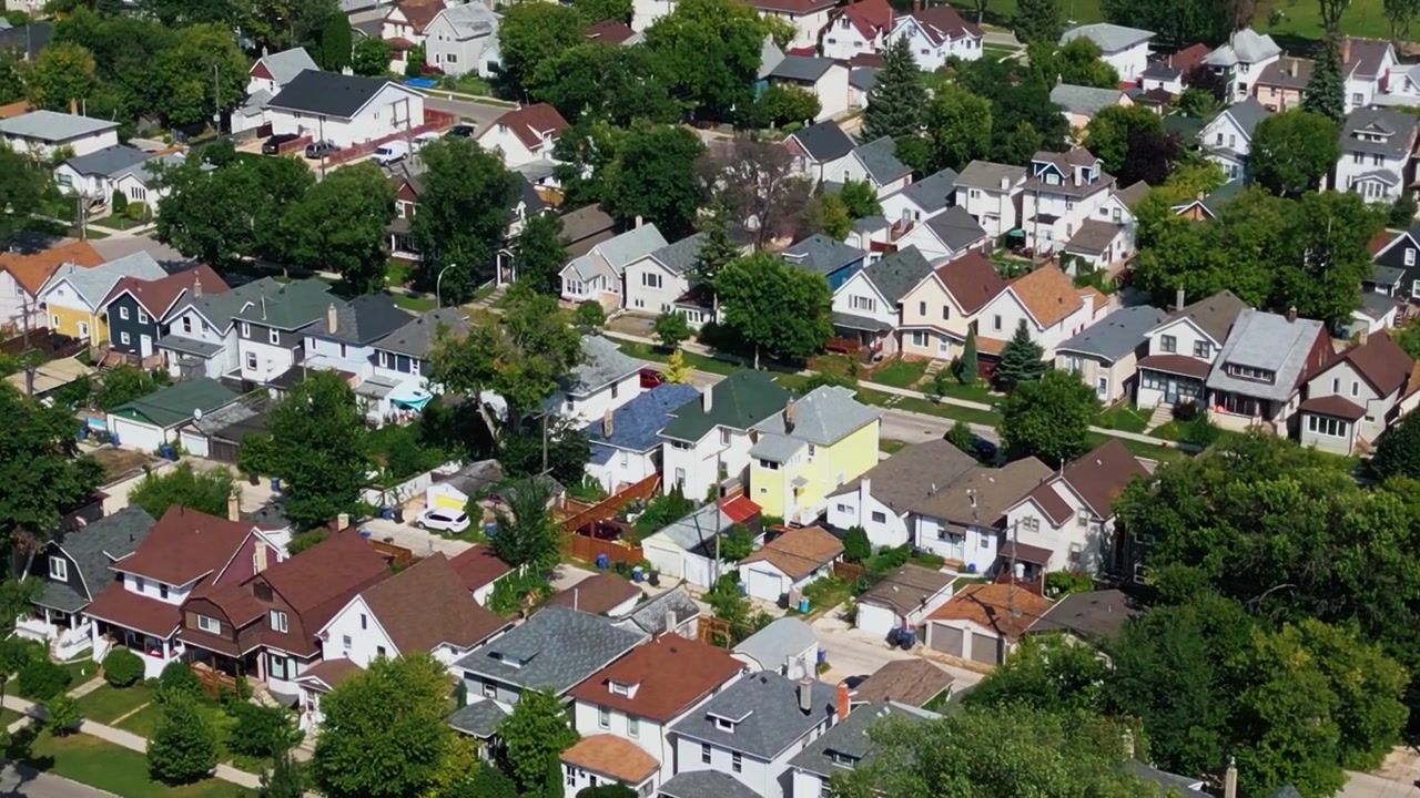 Ampia ripresa aerea con teleobiettivo da drone del centro di Winnipeg, che mostra case unifamiliari colorate, alberi secolari e strade residenziali in una luminosa giornata estiva.