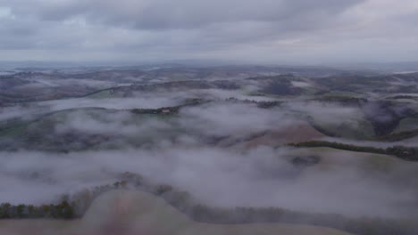 rolling hills of tuscany covered in mist before sunrise, aerial