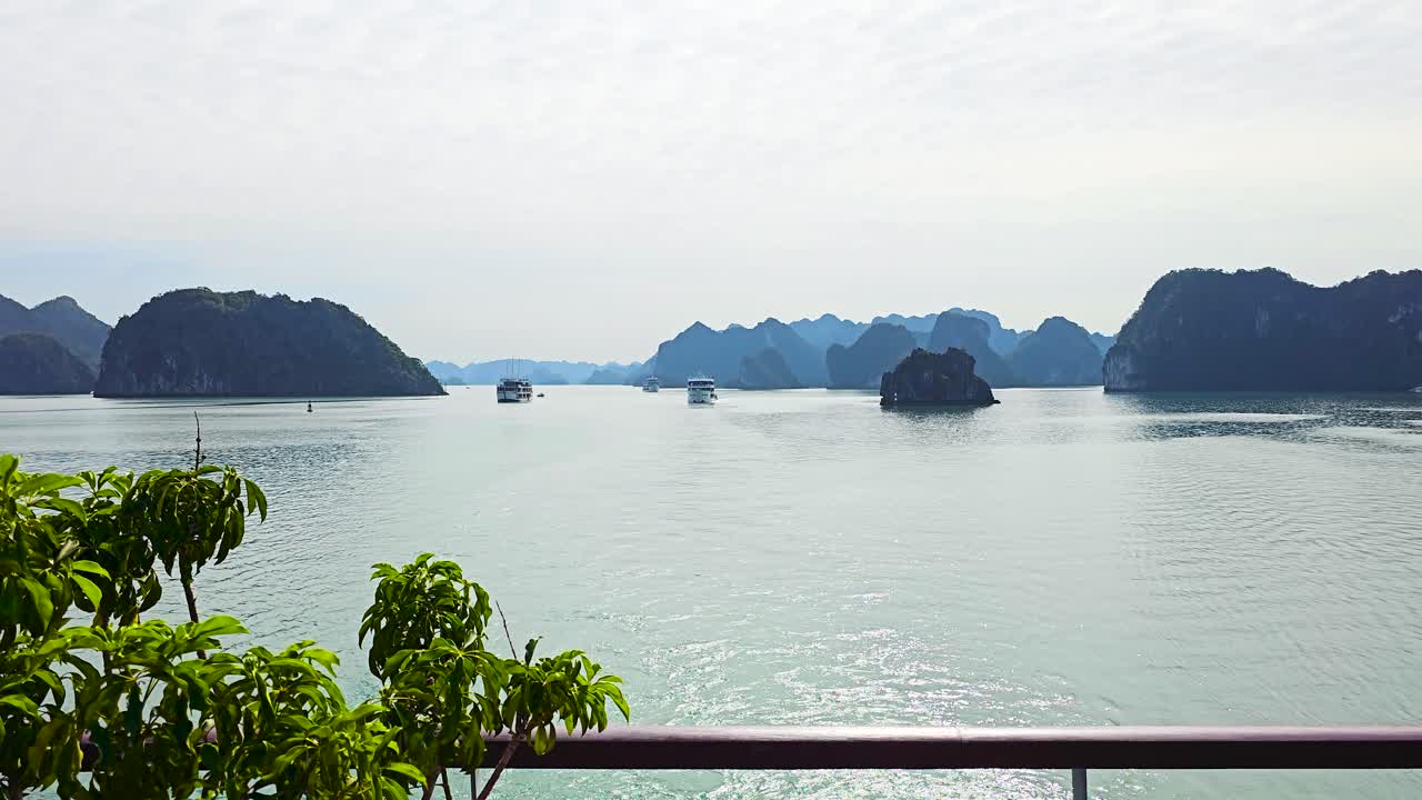 A mesmerizing view of Ha Long Bay's emerald waters dotted with limestone karsts rising dramatically from the sea, captured from a cruise ship's deck with lush foliage framing the tranquil seascape