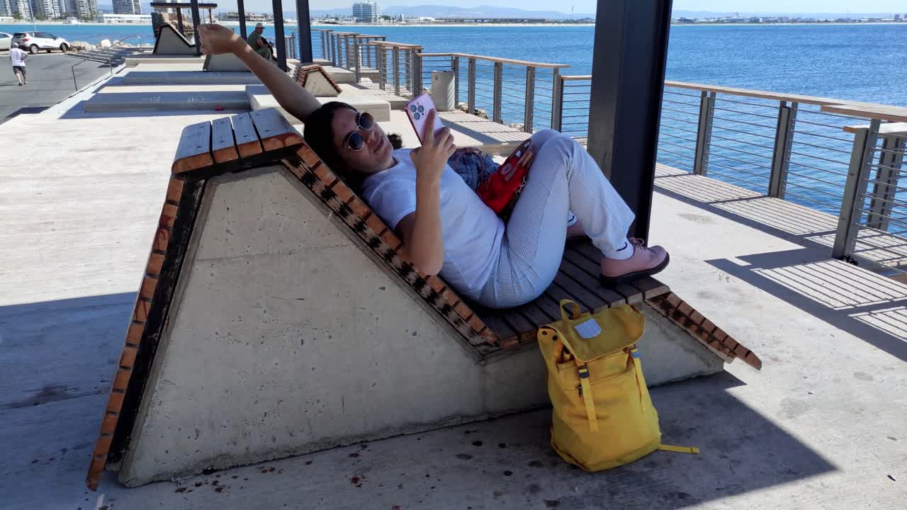 Woman relaxing on modern pier bench using phone