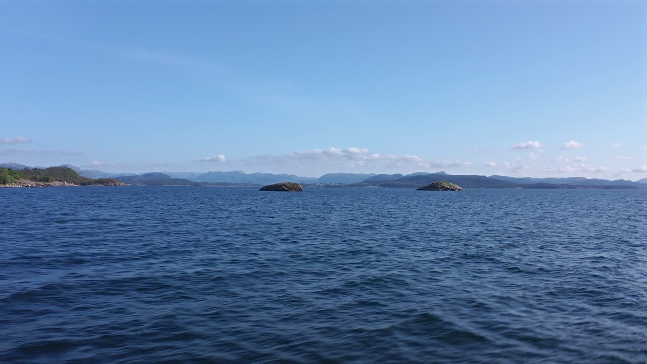 Calm ocean waters with distant islands and mountains in Norway under a clear sky