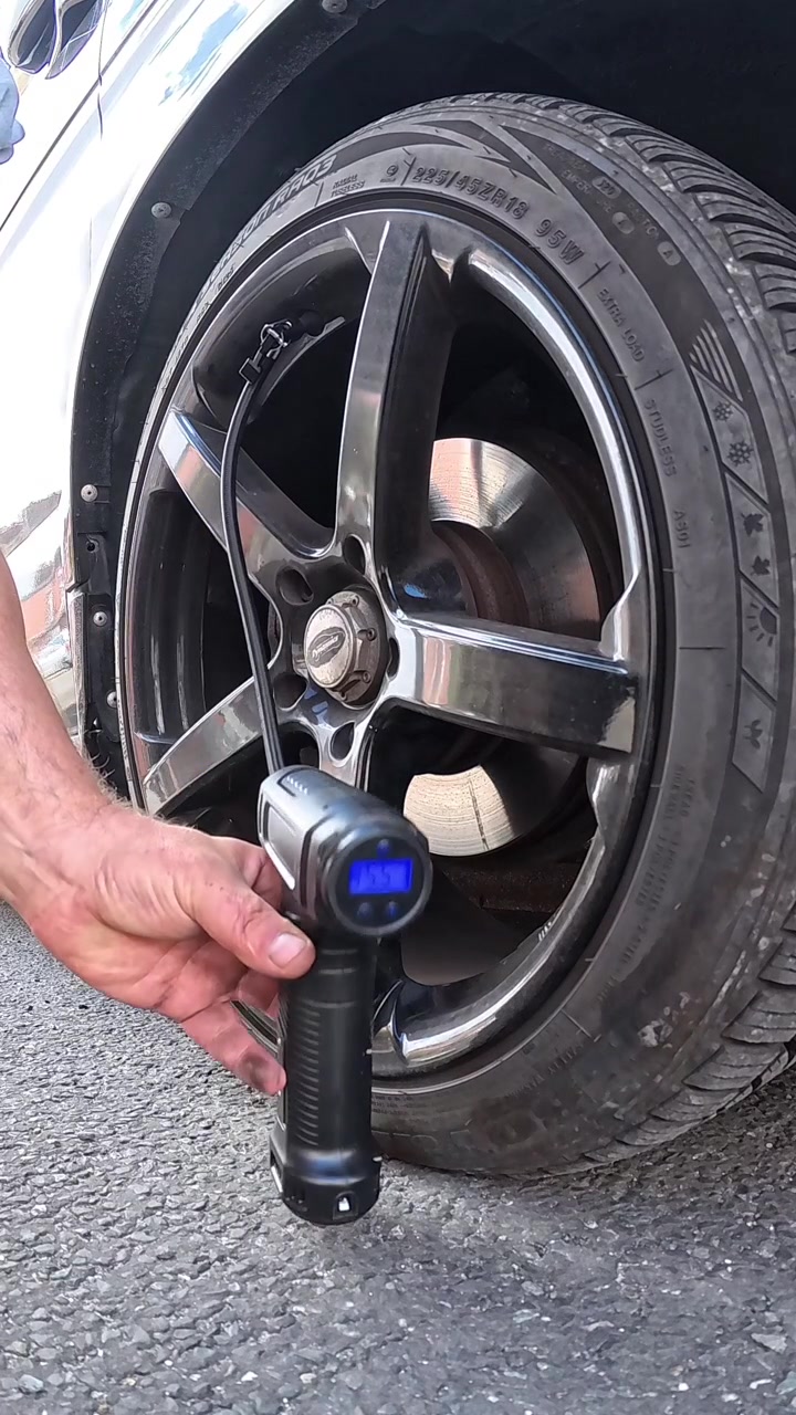Vertical man holding cordless portable air pump to inflate van tyre and checking the pressure