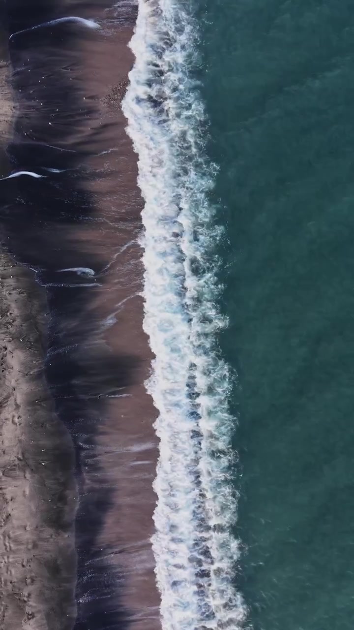 Onde che si infrangono sulla riva di una spiaggia con sabbia scura
