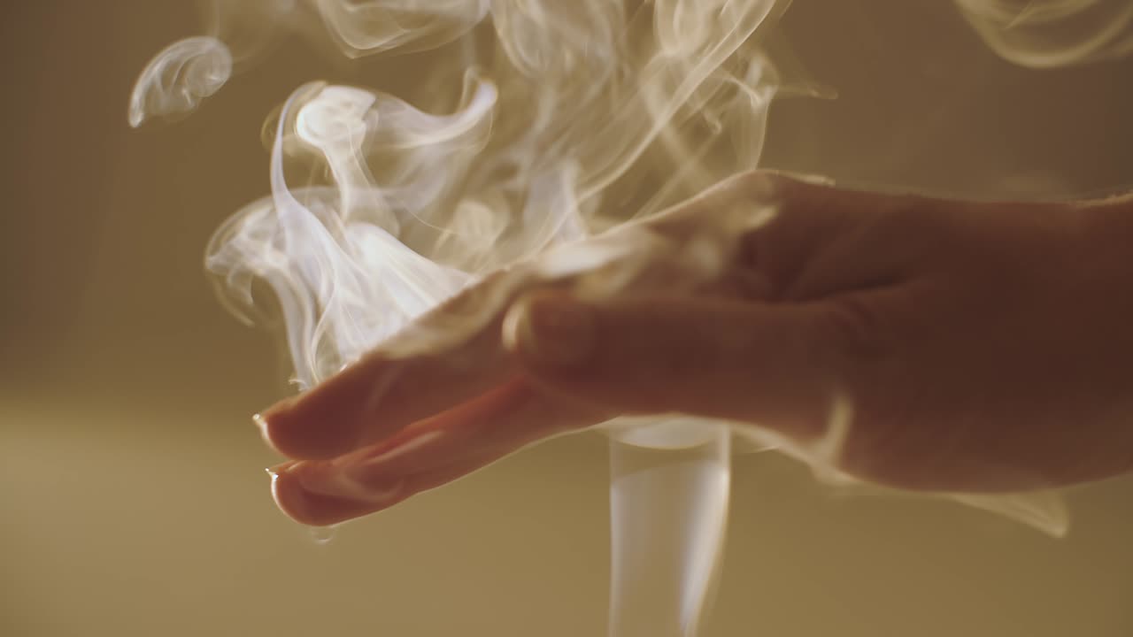 cerca de la mano femenina jugando con el humo de rizado blanco en el interior luz natural cámara lenta. mujer sin rostro acariciando humo de incienso girando en la luz del sol vista de cultivo poco profunda. meditación relajación calma