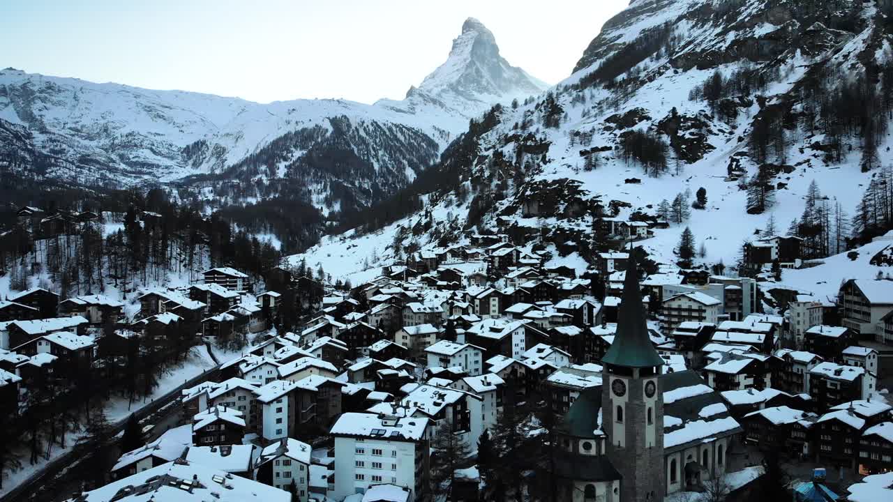 sobrevuelo aéreo sobre el centro de la ciudad de zermatt desde la iglesia hasta el río con vistas al matterhorn durante el invierno