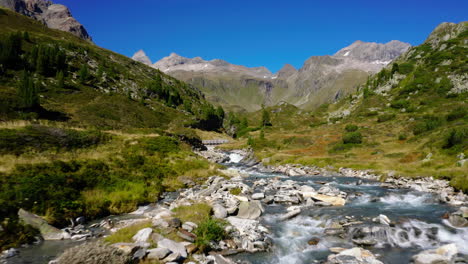 Vista-Aérea-Siguiendo-El-Arroyo-Que-Fluye-A-Través-De-Los-Alpes-De-Zillertal-En-La-Cordillera-De-Los-Valles-Del-Tirol