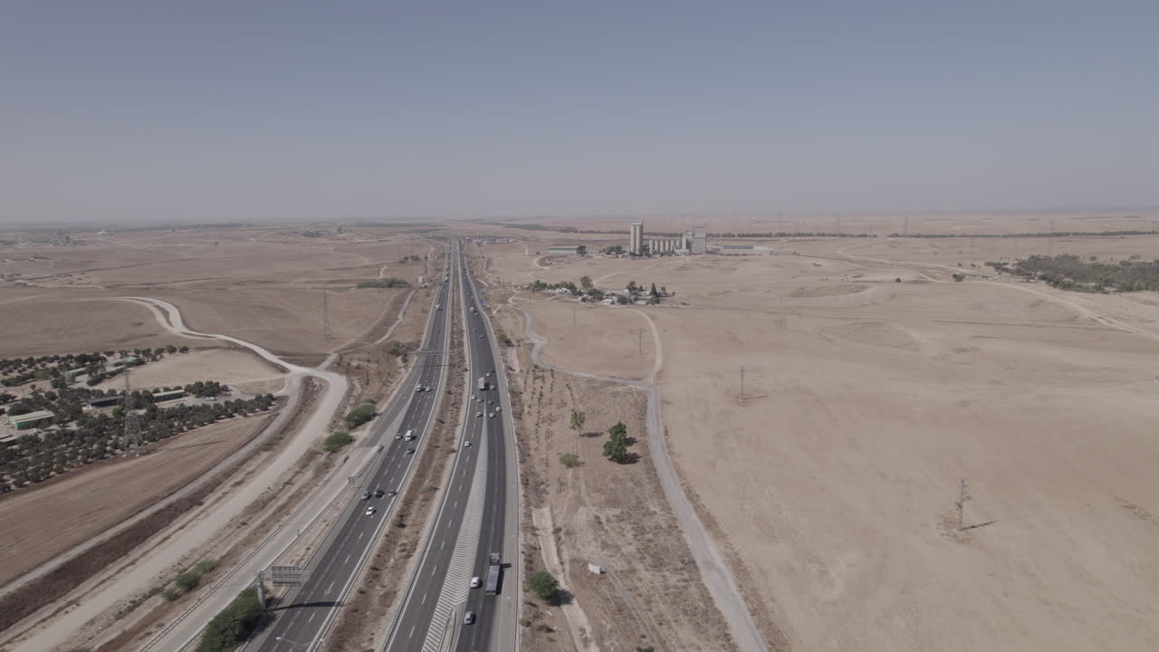 toma aérea cerca de una carretera en una zona seca y desértica, una zona no urbana, los suburbios de la ciudad, algunos edificios de los terratenientes y una antigua fábrica en la distancia