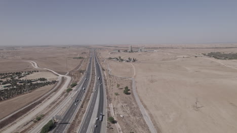 Toma-Aérea-Cerca-De-Una-Carretera-En-Una-Zona-Seca-Y-Desértica,-Un-área-No-Urbana,-Los-Suburbios-De-La-Ciudad,-Algunos-Edificios-De-Los-Terratenientes-Y-Una-Antigua-Fábrica-En-La-Distancia