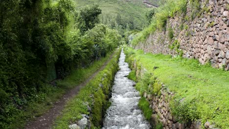 Aerial-shot-of-creek-next-to-a-walking-path-in-Urubamba,-sacred-valley-of-the-incas-located-in-Cusco,-Perú