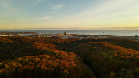 warm sunrise over the city of gdynia on baltic coast in poland with autumn forest trees in foreground - sea tower