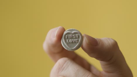 close up of hand holding heart candy avec premier message d'amour sur fond jaune