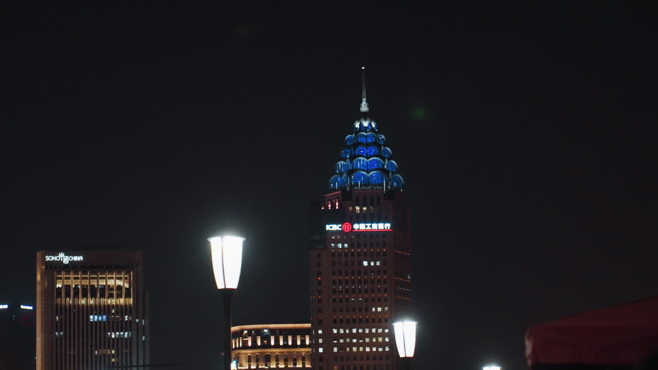 Skyline notturno, torre blu illuminata nel centro, punto panoramico tranquillo sul tetto con lampione luminoso in primo piano, cima di un grattacielo distante immersa in LED blu, bokeh cinematografico e atmosfera dai toni freddi