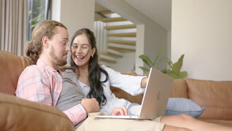 una pareja diversa está disfrutando del tiempo en un sofá con una computadora portátil en casa