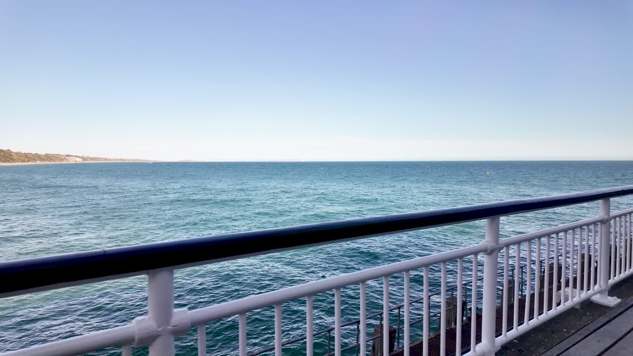 Calm ocean view from a seaside promenade with white railings and clear blue sky today