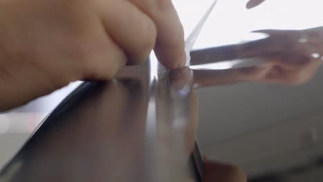 man removing excess paint protection film from car's exterior close up