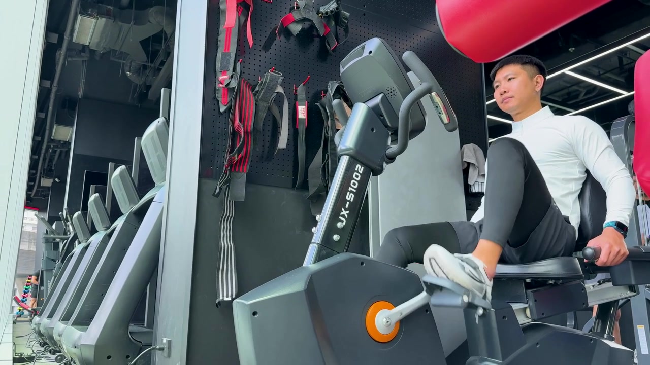 Athletic man training on a recumbent bike inside a bright modern fitness center.