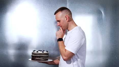 mid-aged caucasian man holding a cake. man looks thoughtfully on the dessert and then shows it to camera.
