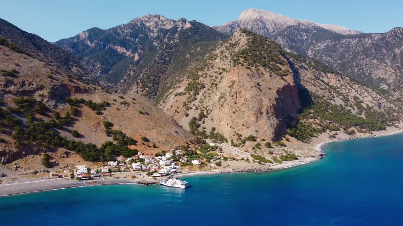 Aerial footage of the ferry at Agia Roumeli, and the final valley at the end of the Samaria Gorge hike. Crete's White Mountains tower above deep blue waters of Libyan Sea - Crete, Greece