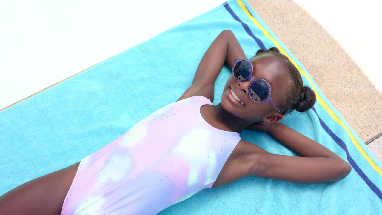 Smiling girl in swimsuit relaxing on towel by pool, enjoying sunny day, copy space