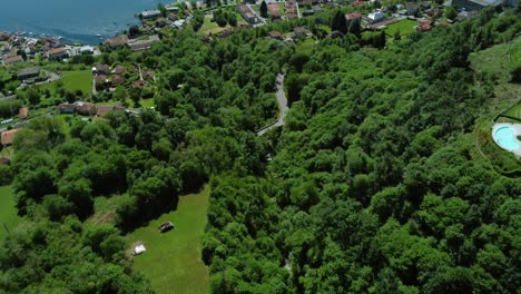 flying over green trees and quaint town on shore of scenic lake orta, italy