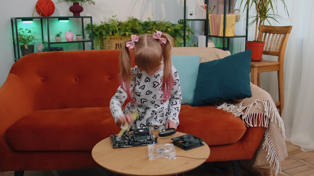 Little girl kid fixing repairing computer mainboard technology part, using magnifying glass at home