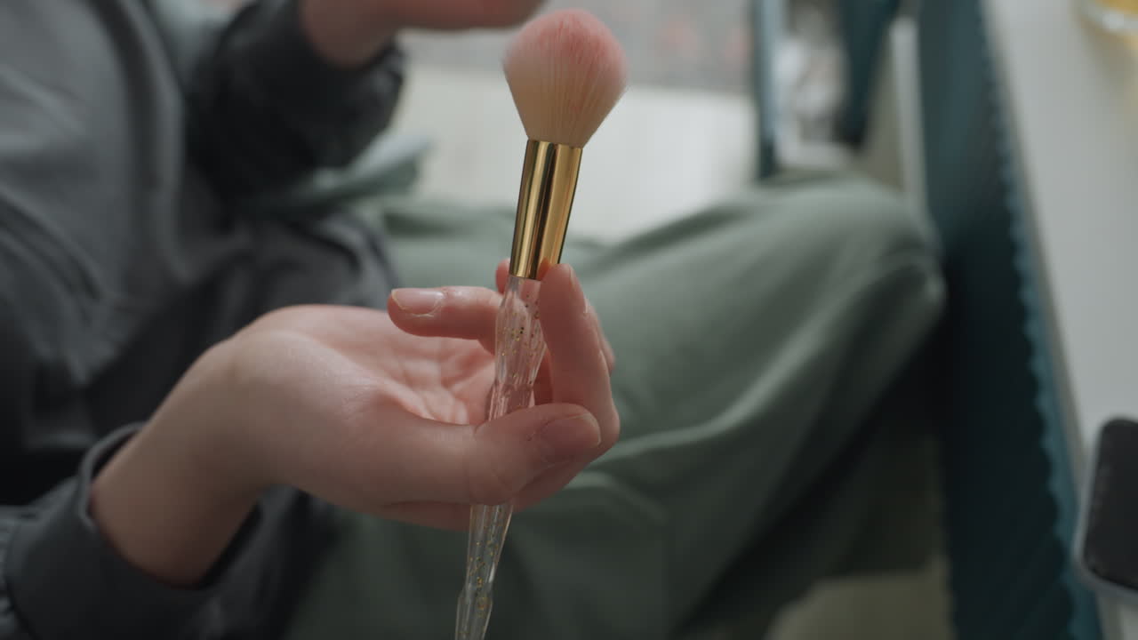 Closeup hand rinsing makeup brush with cascading water droplets pink bristles and golden ferrule catch window light, energetic demo vibe, tactile motion and sparkle, studioadjacent seating, playful