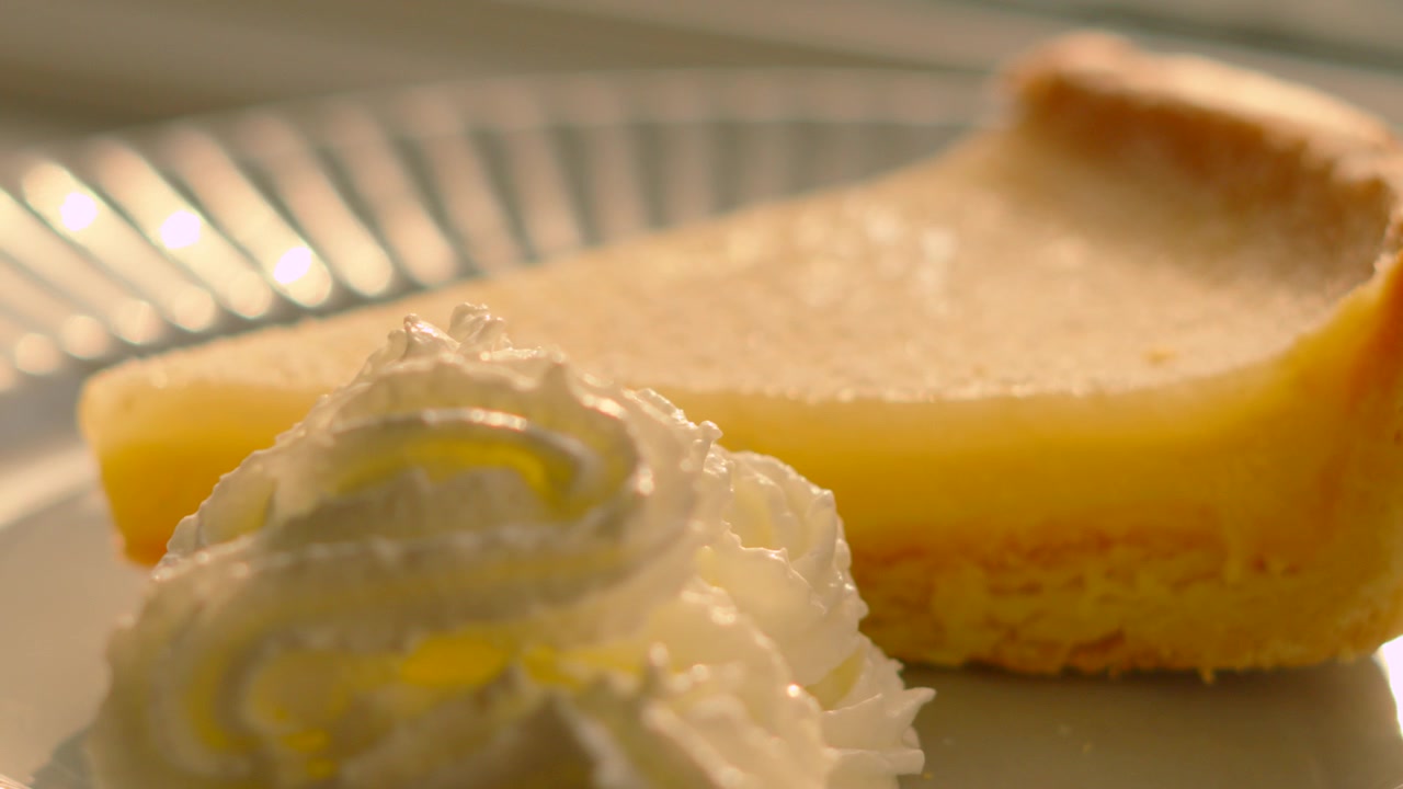 Detailní záběr klasického francouzského citronového koláče (Tarte au Citron) na talíři se šlehačkou. Ideální pro kulinářské aplikace, montáže na sociální média, propagaci luxusních restaurací. 4K.