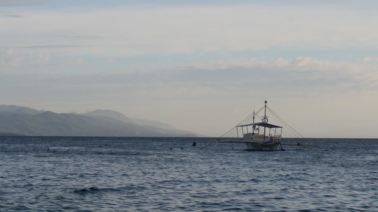 필리핀 세부 섬의 모알보알 시 근처 해가 지는 동안 바다 위를 떠다니는 전통적인 아웃리거 보트