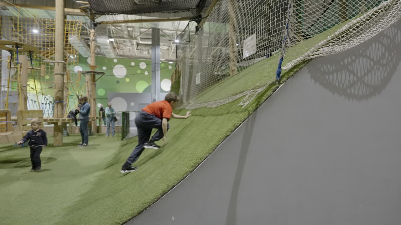 Children playing and climbing on a green slope at an indoor playground