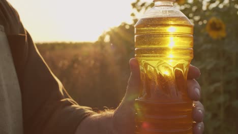 mano sujetando una botella de plástico con aceite de girasol fresco contra el campo de girasol