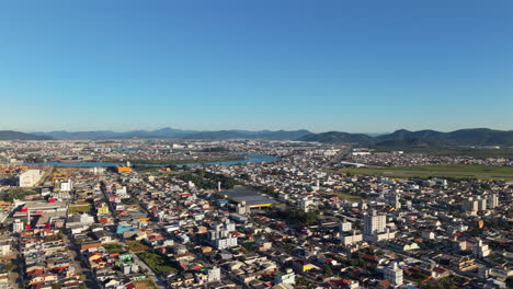 wide aerial view over the city of navegantes, santa catarina, brazil, showing the urban landscape with the runway of navegantes international airport, surrounded by mountains under a clear blue sky