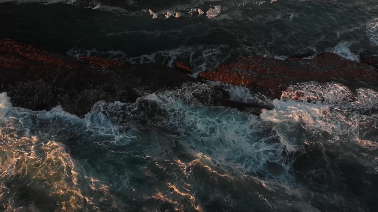 Aerial drone footage capturing ocean waves crashing against a rocky coastline