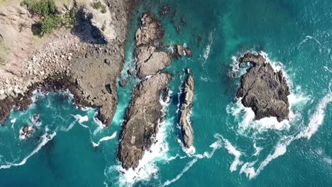 Aerial-shot,-drone-view-looking-above-rotating,-waves-hitting-the-rocks-Medlands-beach,-Great-Barrier-Island,-New-Zealand