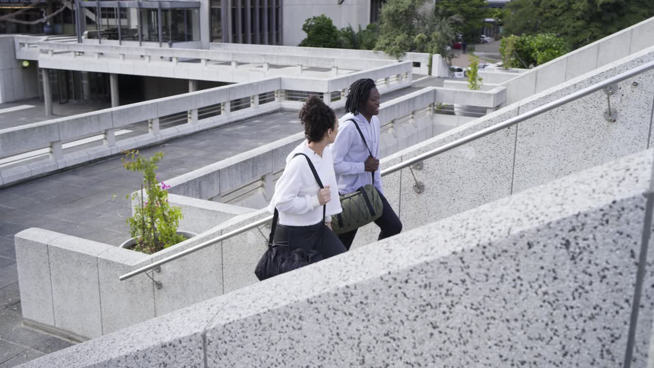 Amigos diversos llegando a unas escaleras, llevando bolsas de viaje, subiendo en una plaza urbana para acceder a la azotea