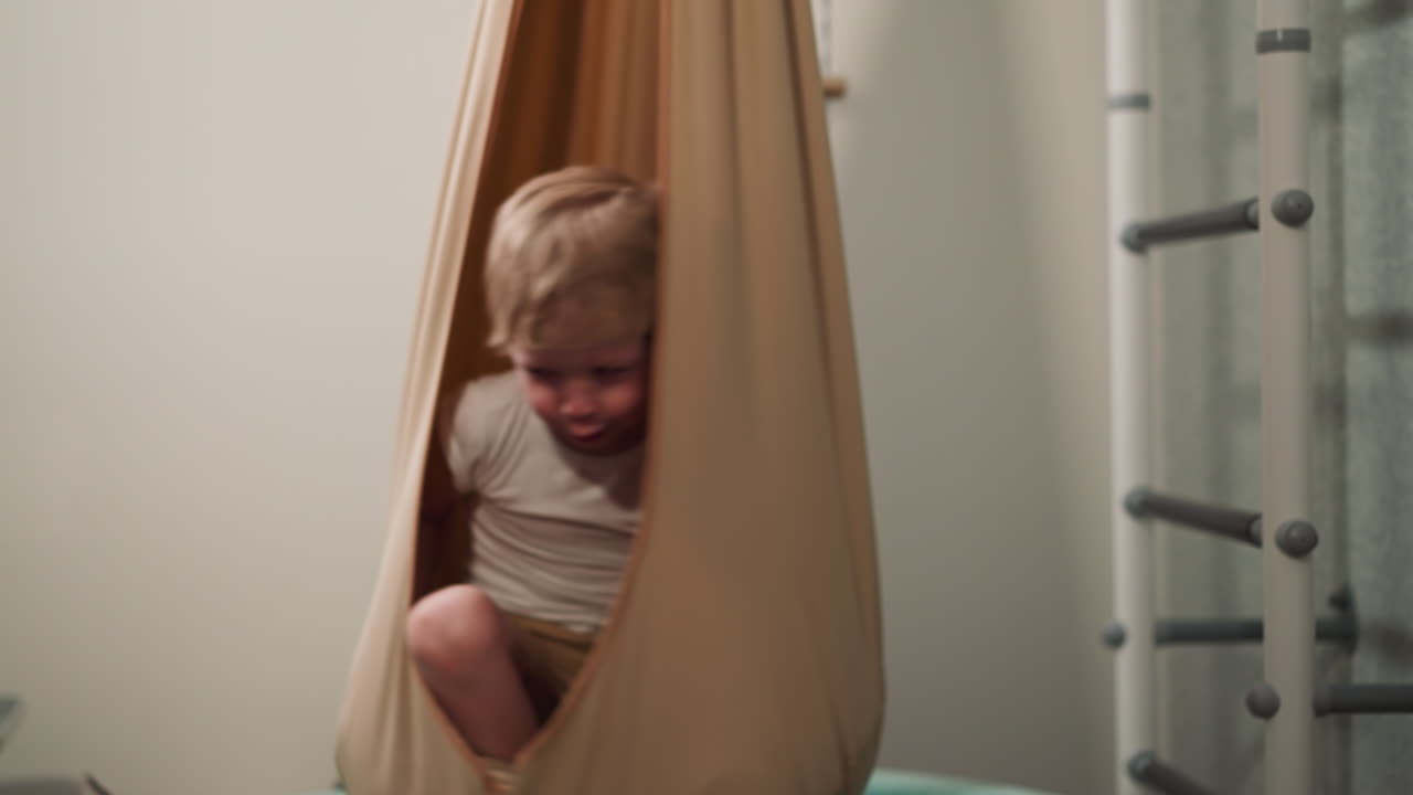 Bambino felice seduto su una sedia amaca girevole in una palestra casalinga.