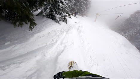 first person view of the snowboard ride by the snowy forest under funicular line. following the fellow snowboarder. sportsman stops as he falls.