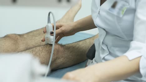 woman doctor hands examines young man patient knee-joint using ultrasound sensor device, sonography. doctor runs ultrasound sensor over patient's leg, knee.