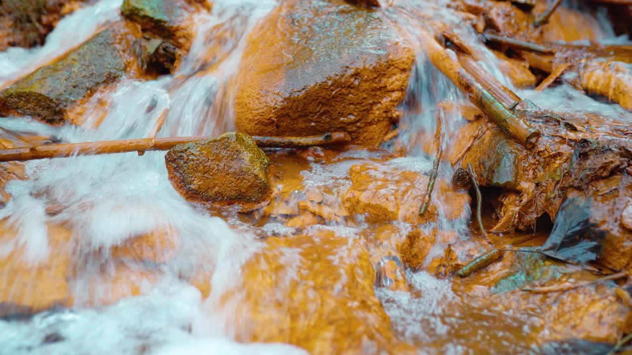 Creek close up in forest with orange colored rocks of Iron-containing sulfur spring water.
